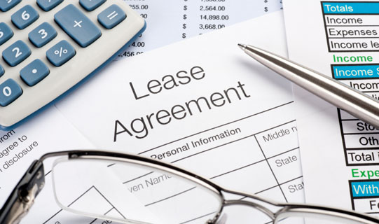 A close-up view of a lease agreement, glasses, calculator, and pen.