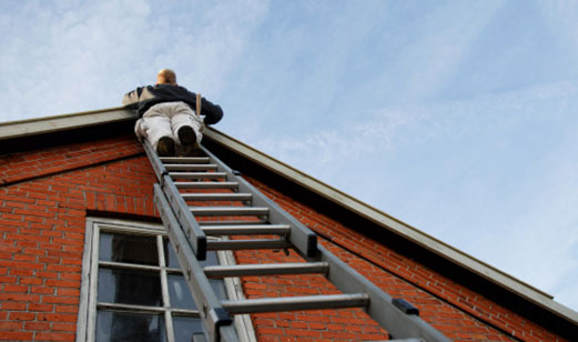 A man on a ladder inspecting the roof.