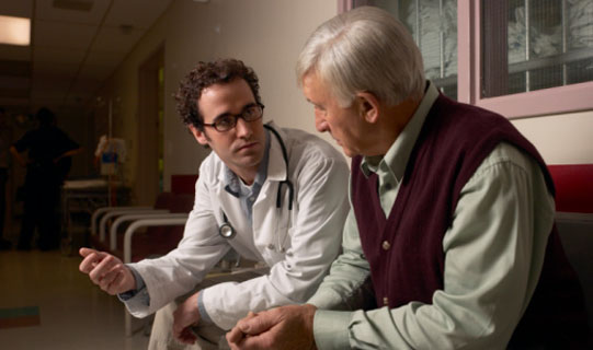 A doctor is talking to an older gentleman in a waiting room.