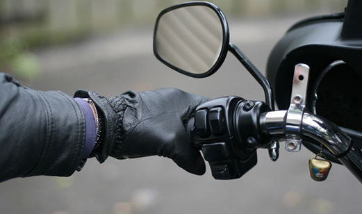 A close-up view of a motorcyclist leather glove hand holding onto the motorcycle handlebar.