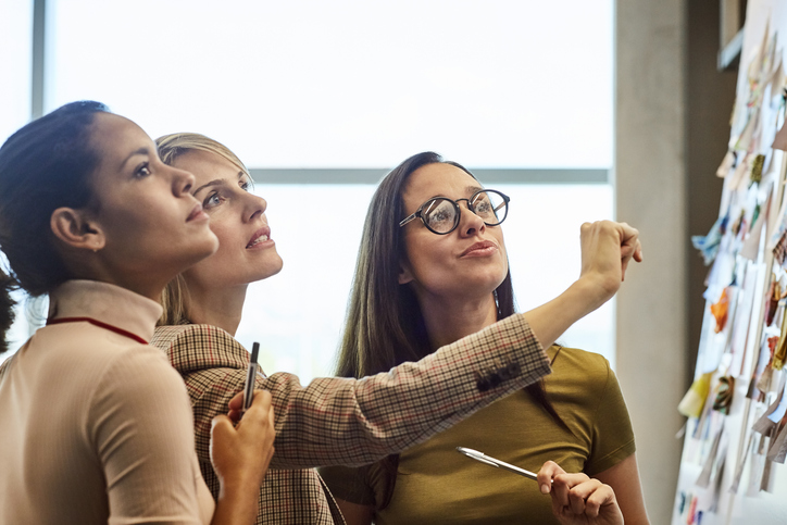 Three women collaborating using post-its on a board.