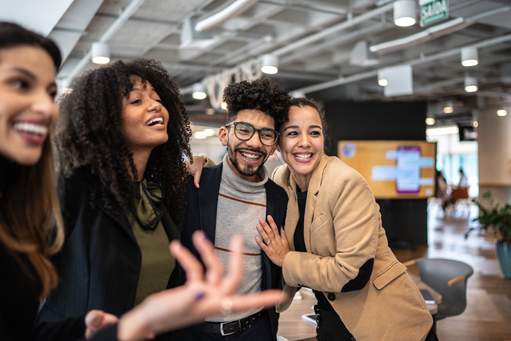 Group of coworkers in an office hugging and smiling.