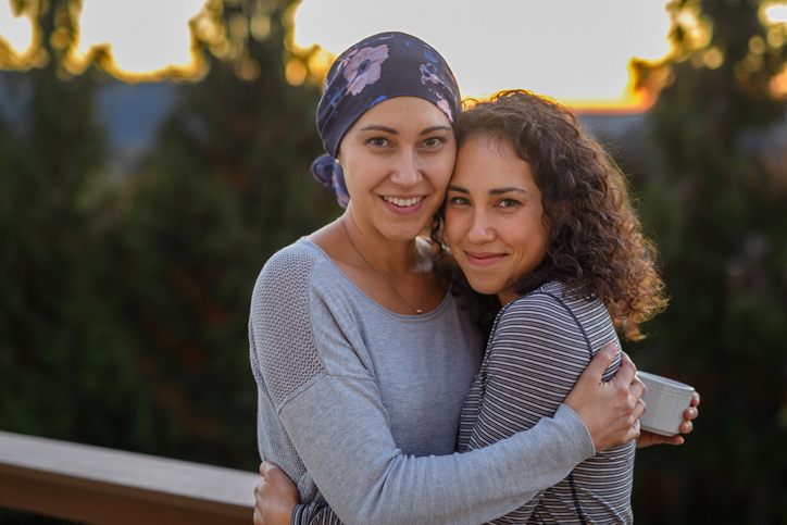 Two women hugging, one with a scarf head wrap.