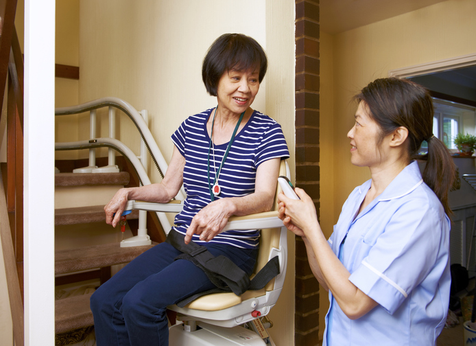 Young woman helping an older woman with a chair lift.