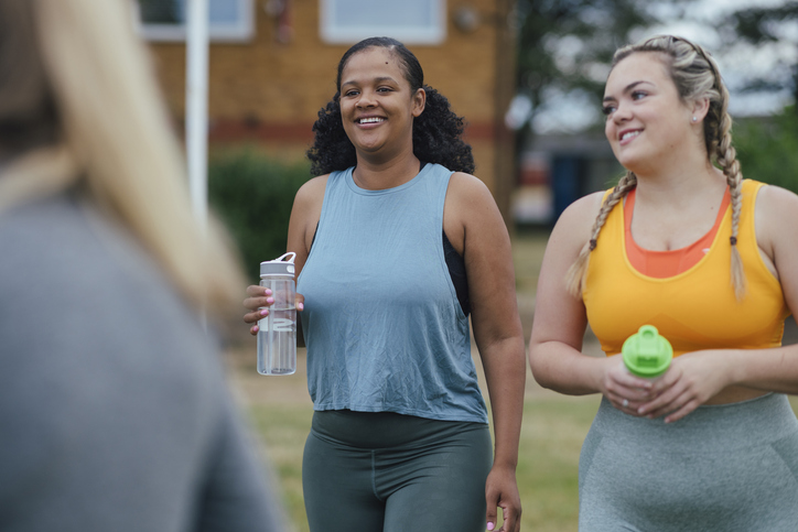 Smiling women drinking water in exercise attire.