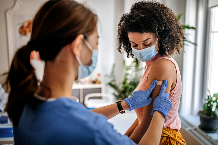 Nurse putting bandaid on woman's arm.