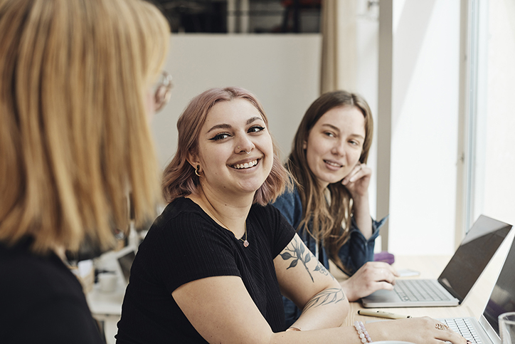 Three women on laptops smiling at each other.