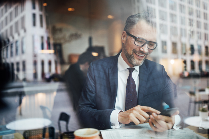 Man looking at phone and smiling in a coffee shop.
