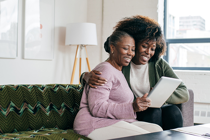 Young woman  embracing senior woman on couch while looking at tablet together