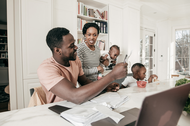 Parents with two young children looking phone and laptop.