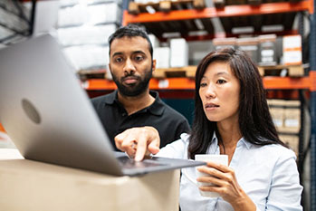 Two people looking at a laptop in a warehouse.
