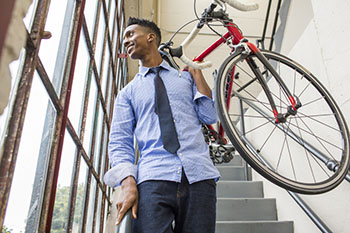 Man in office attire carrying bike down stairs.