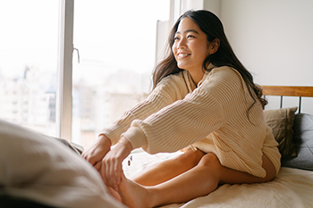 Woman sitting up in bed in the morning, stretching and smiling.