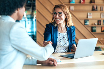 Smiling woman at laptop, shaking hand of another woman.