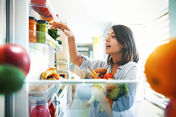 Woman gathering fruit and vegetables from a refrigerator.