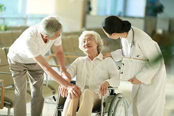Two people helping elderly woman in wheelchair.