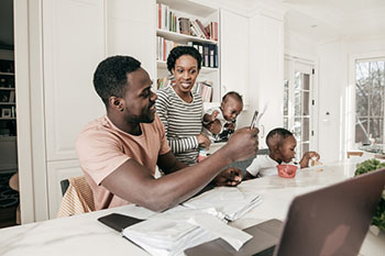 Parents with two young children looking phone and laptop.