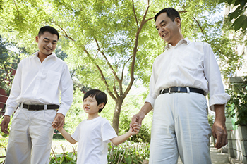 Two fathers holding hands of their son while walking.