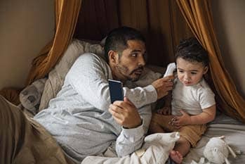 Father taking temperature of baby while on the phone.