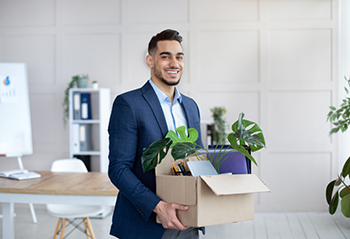 Man in suit holding a box of desk belongings in an office.