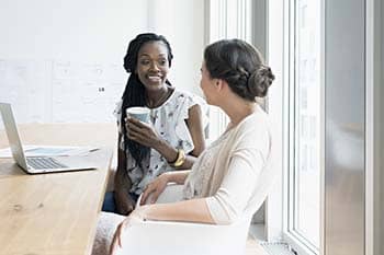 Two women having a conversation in front of a laptop.