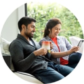 A couple sits on their porch smiling as they look at their tablet. 