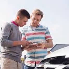 Two men exchanging information over a car hood.