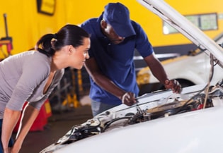 An auto service professional and a customer look under the car hood. 