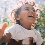 A toddler is smiling while he plays outside. 