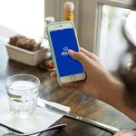 A woman sitting at a table opens the Allstate&reg; mobile app on her phone. 