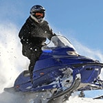 A person in winter gear rides a snowmobile on a snowy slope.  