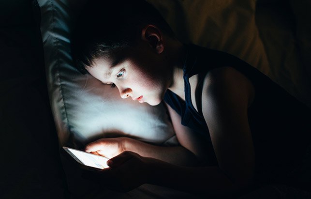 Boy laying in bed while using his tablet. 