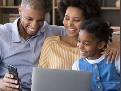 A young family looking at a phone and laptop on a couch. 