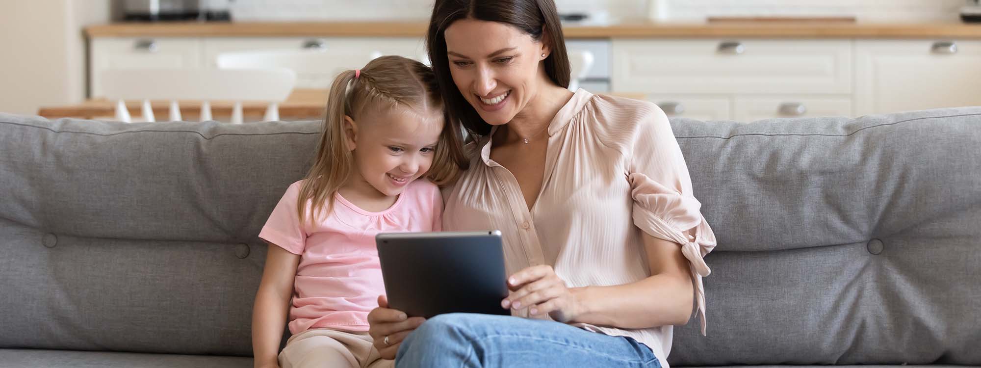 A mother sitting on a couch with her daughter looking at a laptop.  