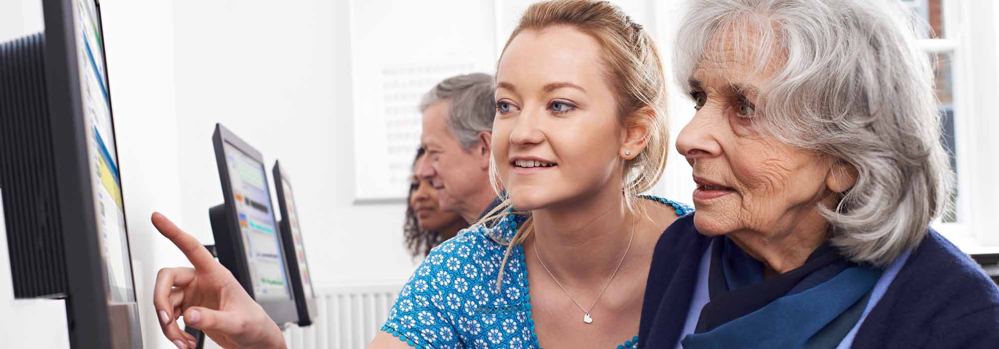 A young woman helping an older woman with her computer.  