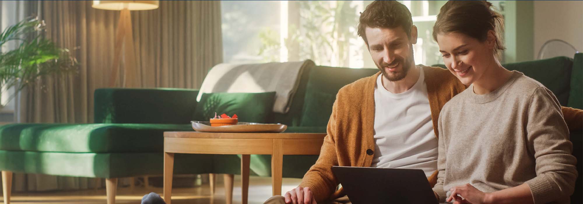 A young couple sitting on the floor in the living room looking at laptop.  