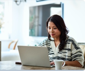 Woman sitting at table looking at laptop. 