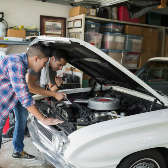 father and song working on engine of classic car.  