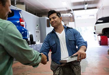 Body shop worker shaking hands with a customer at a collision repair shop. 