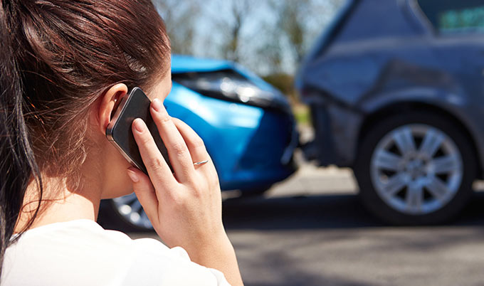 Woman making a phone call while looking at two cars that have been involved in a crash. 