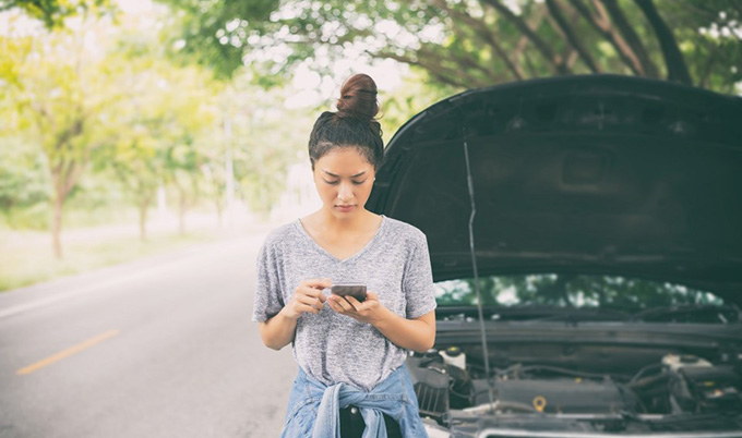 Young woman making call on cellphone in front of car with hood up. 