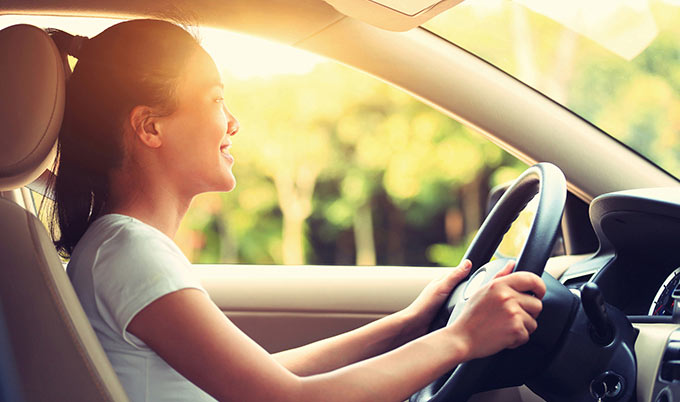 Young woman driving car in sunlight. 