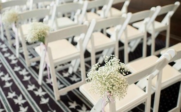 Rows of white chairs with flowers. 
