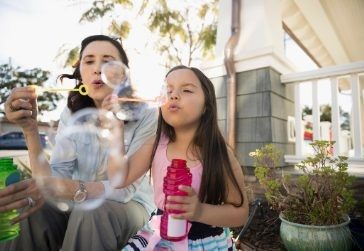 Grandmother and granddaughter outside of house blowing bubbles.