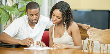 Couple sitting at kitchen table using a calculator. 