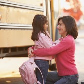 Little girl and mom standing near school bus.