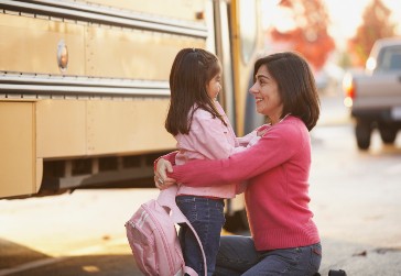 Little girl and mom standing near school bus.