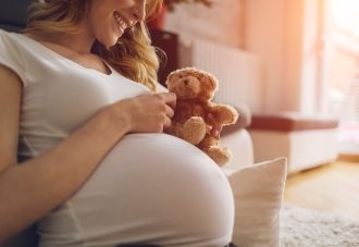 Smiling pregnant woman holding teddy bear. 