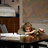 Man sitting at a desk holding a toy motorcycle.. 