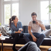 Young woman and man laughing and drinking coffee in apartment living room.  